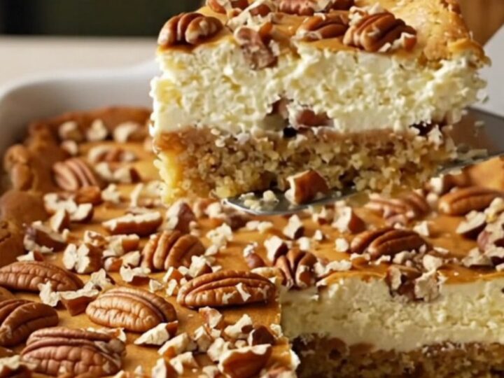 A golden-brown Butter Pecan Gooey Butter Cake in a white rectangular ceramic dish, topped with toasted pecans.