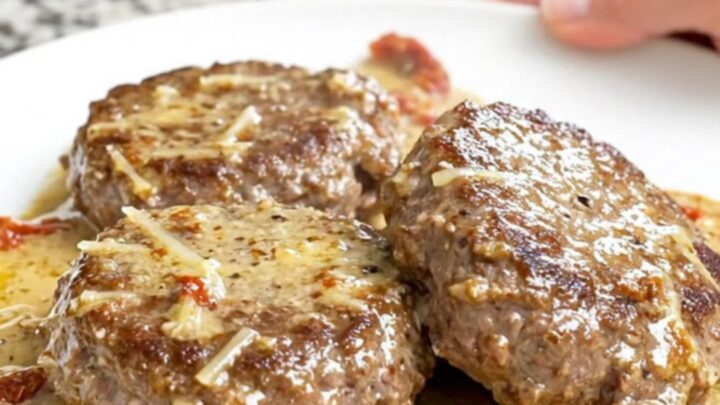 A top-down view of thick, juicy hamburger steaks in a slow cooker topped with sun-dried tomatoes and a creamy sauce.