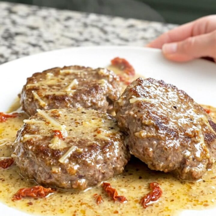 A top-down view of thick, juicy hamburger steaks in a slow cooker topped with sun-dried tomatoes and a creamy sauce.