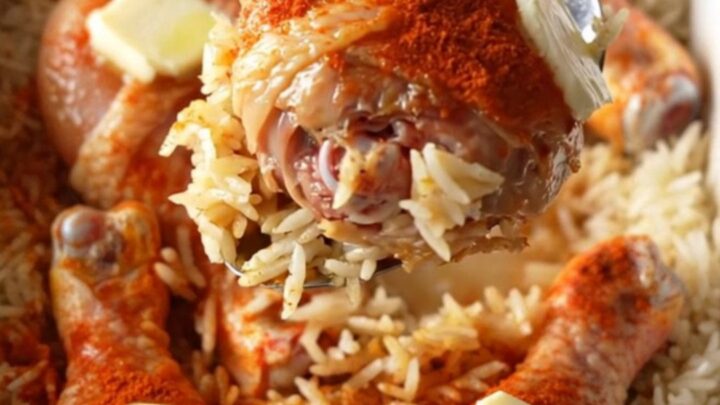 A top-down view of raw chicken drumsticks rubbed with red paprika sitting on a bed of white rice in a white baking dish.