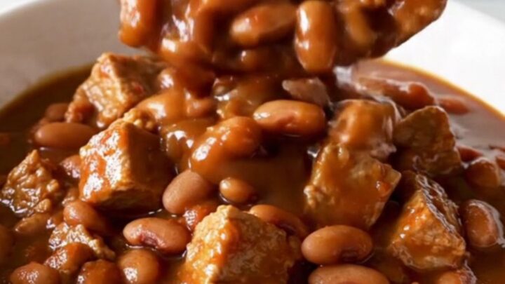 A bowl of slow-cooked pork and beans in a rich, dark molasses sauce with visible tender cubes of pork.
