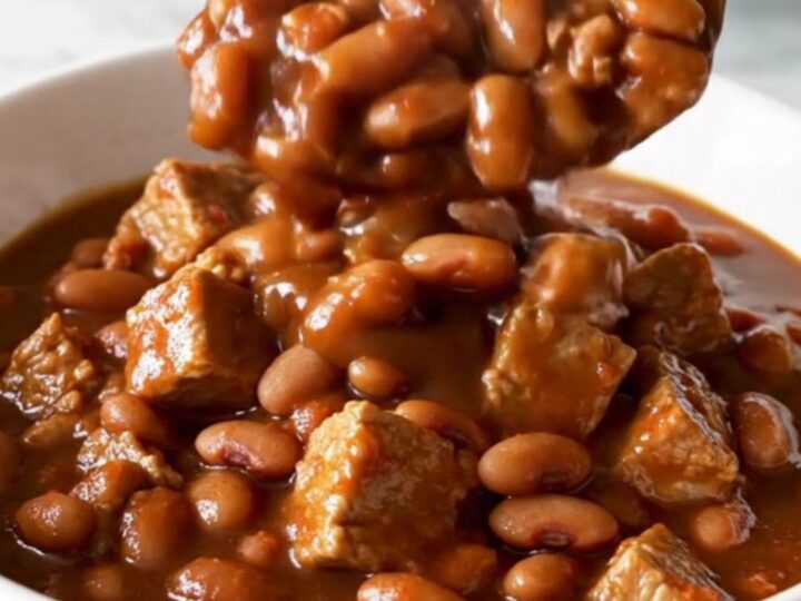 A bowl of slow-cooked pork and beans in a rich, dark molasses sauce with visible tender cubes of pork.
