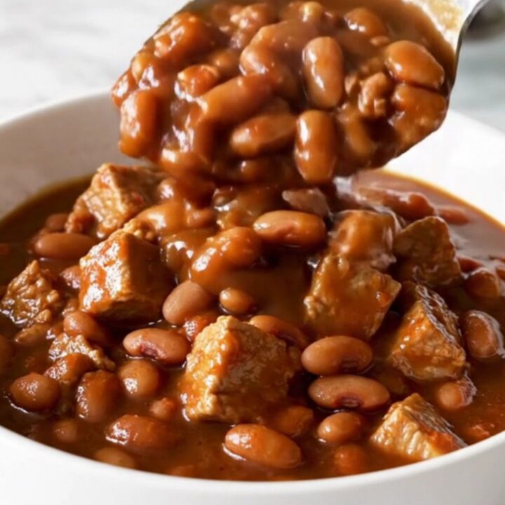 A bowl of slow-cooked pork and beans in a rich, dark molasses sauce with visible tender cubes of pork.