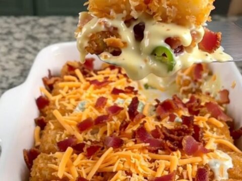 A golden-brown potato tot casserole in a white dish, topped with melted cheddar cheese and crispy bacon.