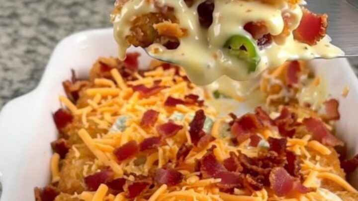 A golden-brown potato tot casserole in a white dish, topped with melted cheddar cheese and crispy bacon.