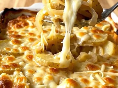 A golden-brown, bubbling French onion potato gratin in a white ceramic baking dish on a wooden counter.