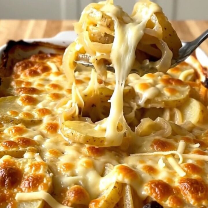 A golden-brown, bubbling French onion potato gratin in a white ceramic baking dish on a wooden counter.
