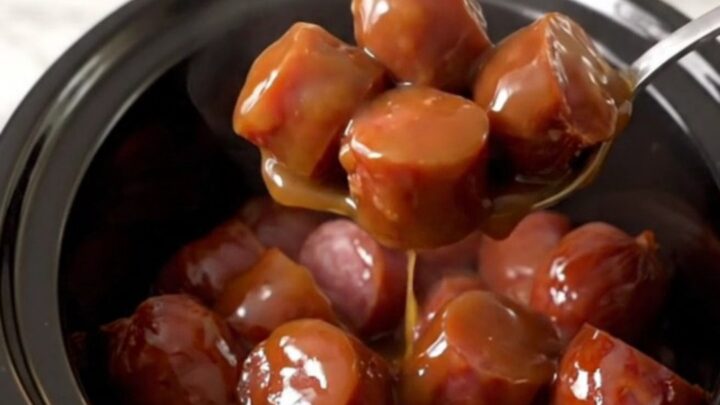 A close-up of thick, glazed kielbasa chunks in a slow cooker, glistening with a dark