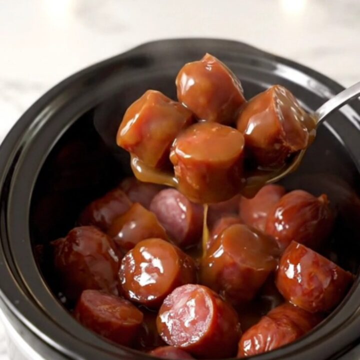 A close-up of thick, glazed kielbasa chunks in a slow cooker, glistening with a dark