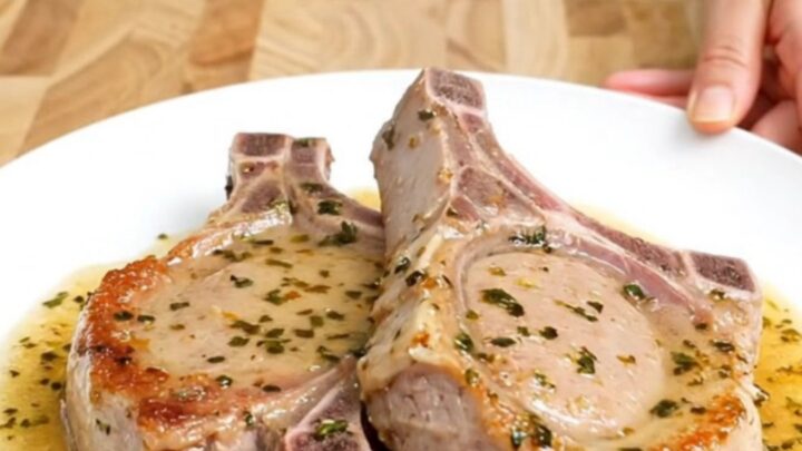 A close-up of tender boneless pork chops in a white slow cooker insert, glazed in a savory-sweet brown sugar and herb sauce.
