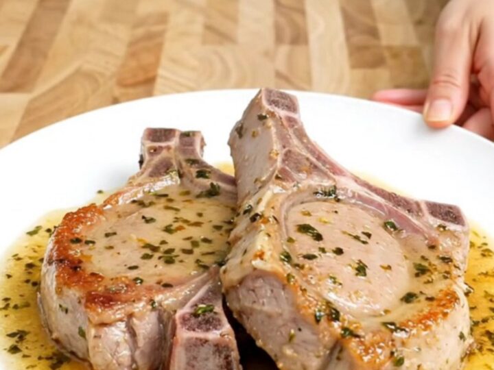 A close-up of tender boneless pork chops in a white slow cooker insert, glazed in a savory-sweet brown sugar and herb sauce.