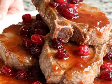Slow-cooked boneless pork chops coated in a rich, glossy cranberry chili sauce on a white plate.