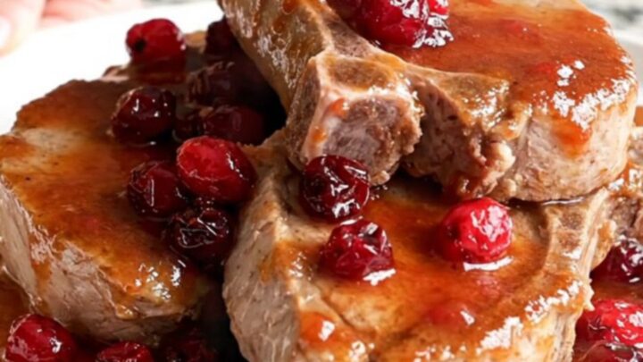 Slow-cooked boneless pork chops coated in a rich, glossy cranberry chili sauce on a white plate.