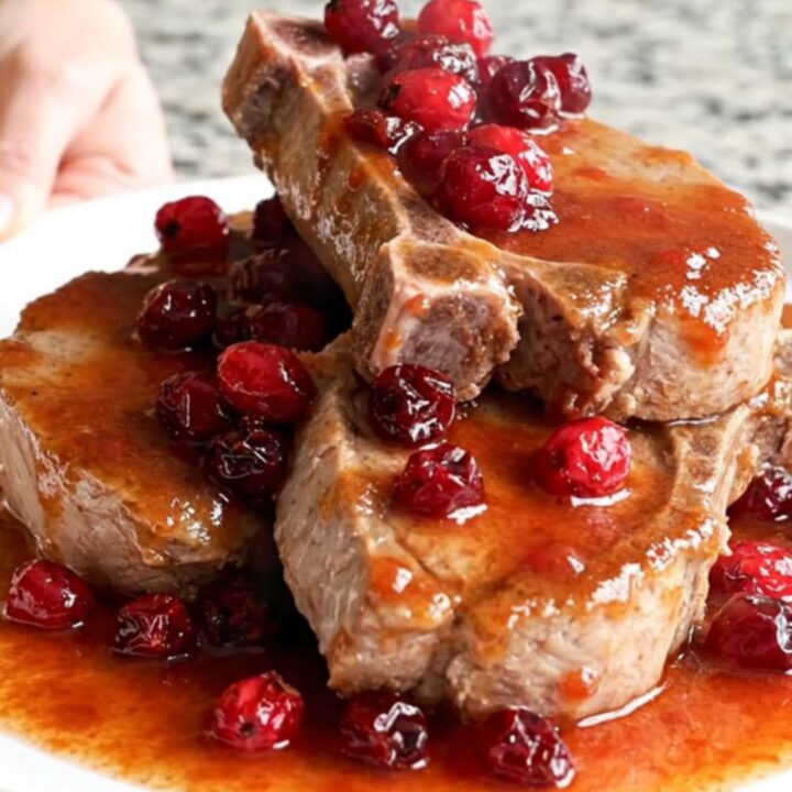 Slow-cooked boneless pork chops coated in a rich, glossy cranberry chili sauce on a white plate.
