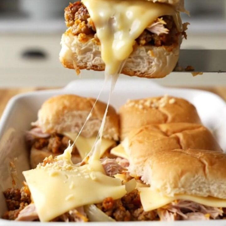 A golden-brown tray of turkey patty melt sliders with melted Swiss cheese and toasted onion tops.