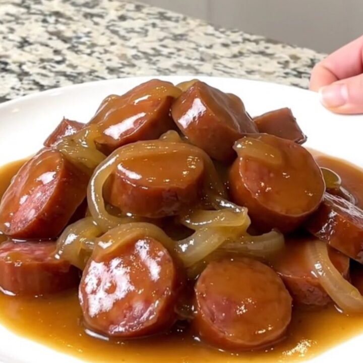 A close-up of a slow cooker filled with sliced smoked sausage, cubed gold potatoes, and onions in a rich