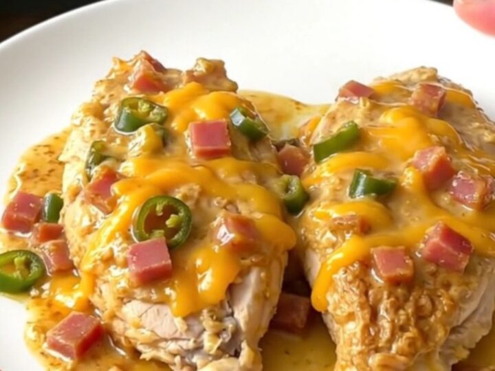 A top-down view of creamy Mississippi Sin Chicken in a slow cooker with melted cheese and ham.