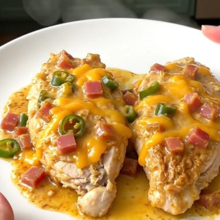 A top-down view of creamy Mississippi Sin Chicken in a slow cooker with melted cheese and ham.
