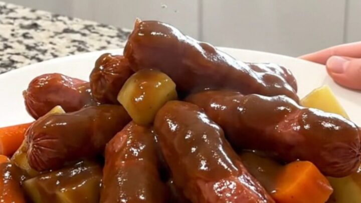 A rustic, overhead shot of a slow cooker filled with kielbasa, potatoes, and carrots in a rich gravy.