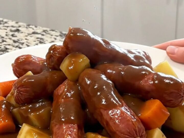 A rustic, overhead shot of a slow cooker filled with kielbasa, potatoes, and carrots in a rich gravy.