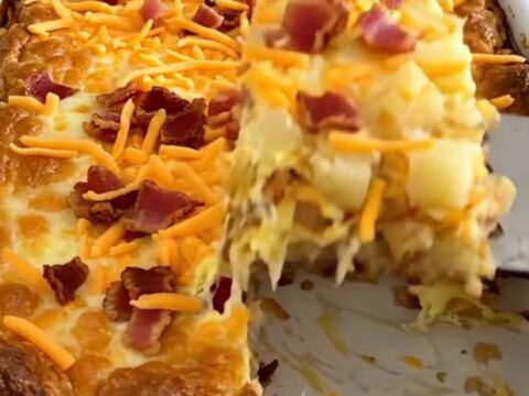 A golden-brown baked breakfast casserole in a white dish, topped with melted cheddar and bacon.