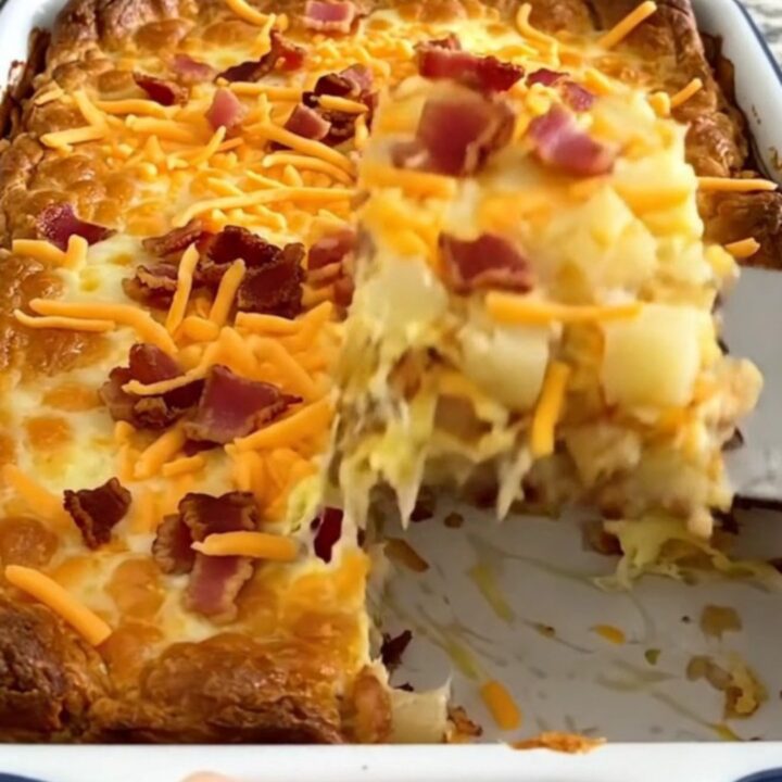 A golden-brown baked breakfast casserole in a white dish, topped with melted cheddar and bacon.
