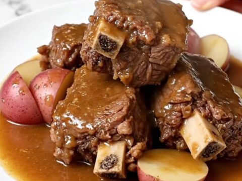 A plate featuring tender bone-in beef short ribs with halved red potatoes and onion gravy.