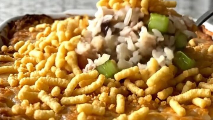 A top-down view of a rectangular baking dish filled with rice, turkey, celery, and a crispy noodle topping.