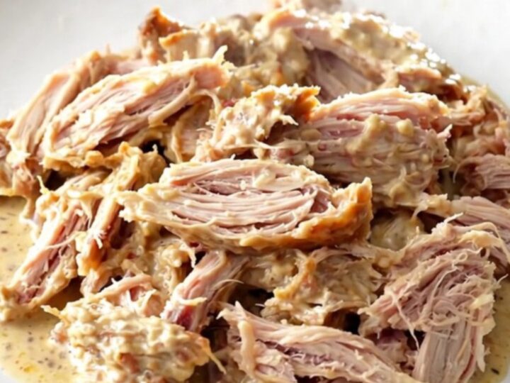 A close-up of shredded turkey tenderloins coated in a rich, creamy Italian sauce on a white plate.