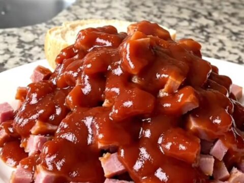 A close-up of a pile of tender chipped ham coated in a rich, tangy red barbecue sauce in a slow cooker.