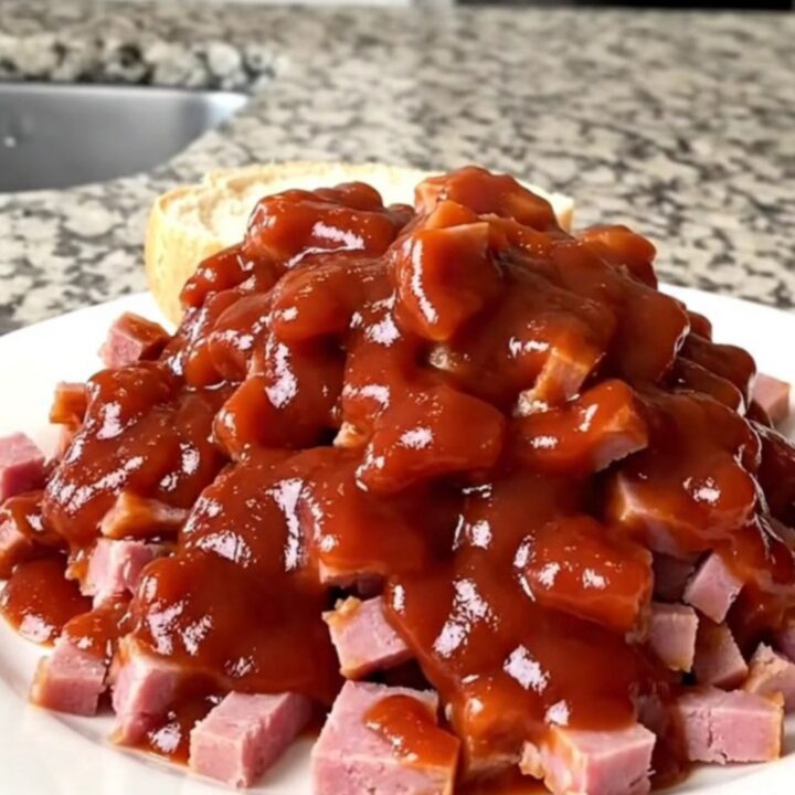 A close-up of a pile of tender chipped ham coated in a rich, tangy red barbecue sauce in a slow cooker.