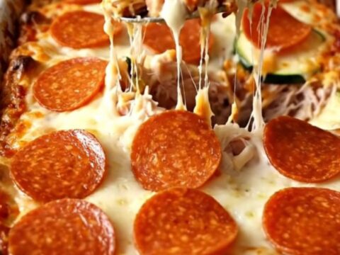 A golden, bubbling zucchini pizza casserole with pepperoni and melted cheese in a white dish.