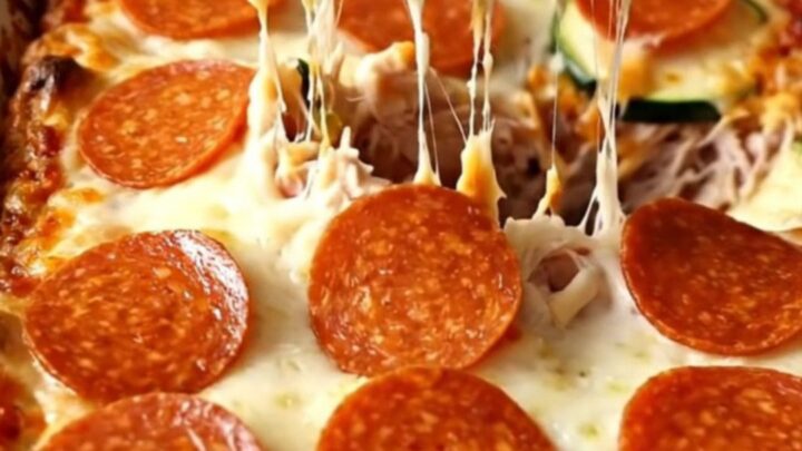 A golden, bubbling zucchini pizza casserole with pepperoni and melted cheese in a white dish.