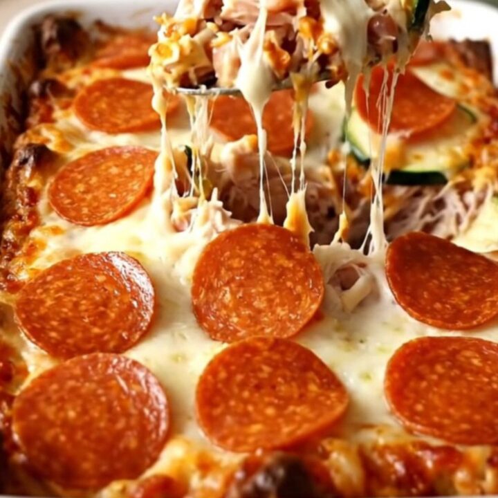 A golden, bubbling zucchini pizza casserole with pepperoni and melted cheese in a white dish.