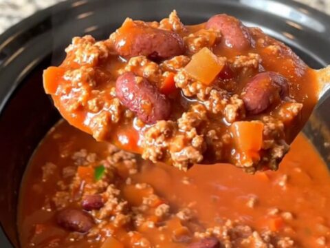 A bowl of hearty beef chili with kidney beans and jalapenos in a slow cooker, featuring a rich red tomato sauce.