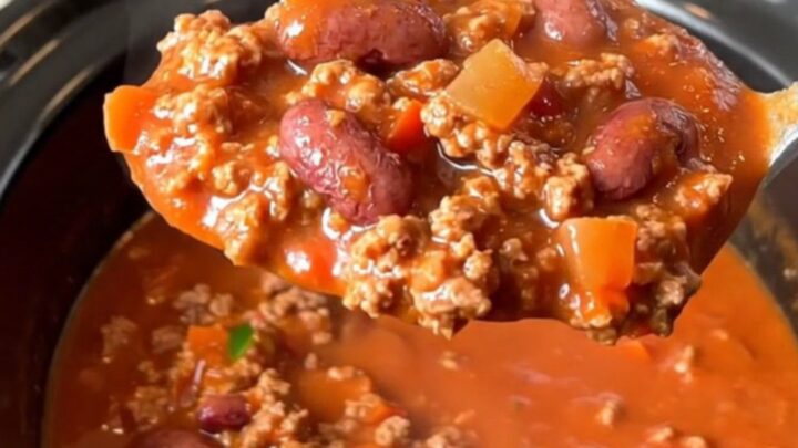 A bowl of hearty beef chili with kidney beans and jalapenos in a slow cooker, featuring a rich red tomato sauce.