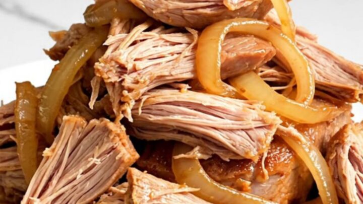 A close-up of tender, shredded orange soda pulled pork on a white plate with visible onions.
