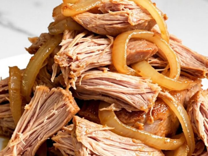 A close-up of tender, shredded orange soda pulled pork on a white plate with visible onions.