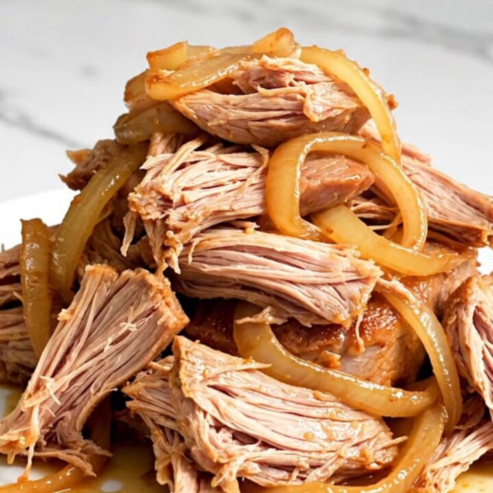 A close-up of tender, shredded orange soda pulled pork on a white plate with visible onions.