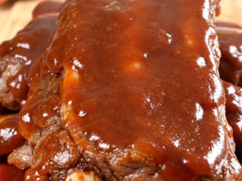 A close-up view of tender, slow-cooked beef back ribs coated in a rich, glossy barbecue sauce on a dark background.