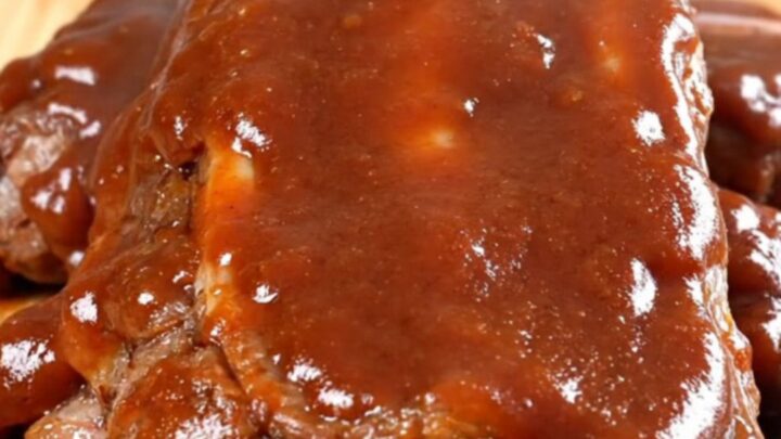 A close-up view of tender, slow-cooked beef back ribs coated in a rich, glossy barbecue sauce on a dark background.