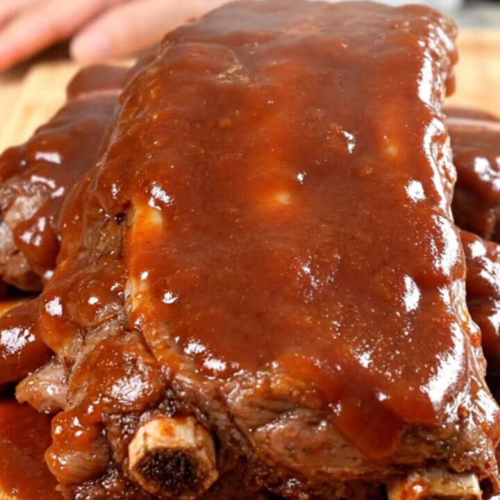 A close-up view of tender, slow-cooked beef back ribs coated in a rich, glossy barbecue sauce on a dark background.
