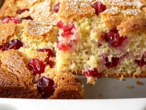 A square of golden cranberry Christmas cake with a visible sugar crust and whole red cranberries inside.