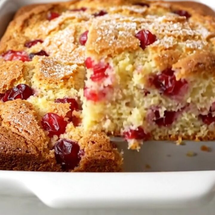 A square of golden cranberry Christmas cake with a visible sugar crust and whole red cranberries inside.