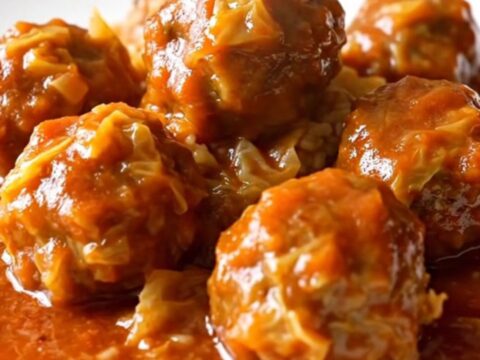 A white ceramic slow cooker filled with turkey meatballs, chopped green cabbage, and a rich red tomato sauce.