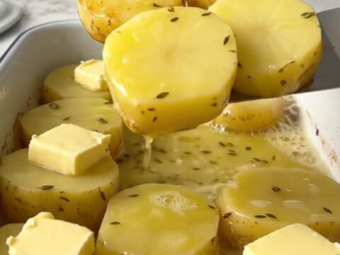 A top-down view of golden-brown melting potatoes in a white rectangular baker with fresh herbs.