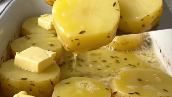 A top-down view of golden-brown melting potatoes in a white rectangular baker with fresh herbs.