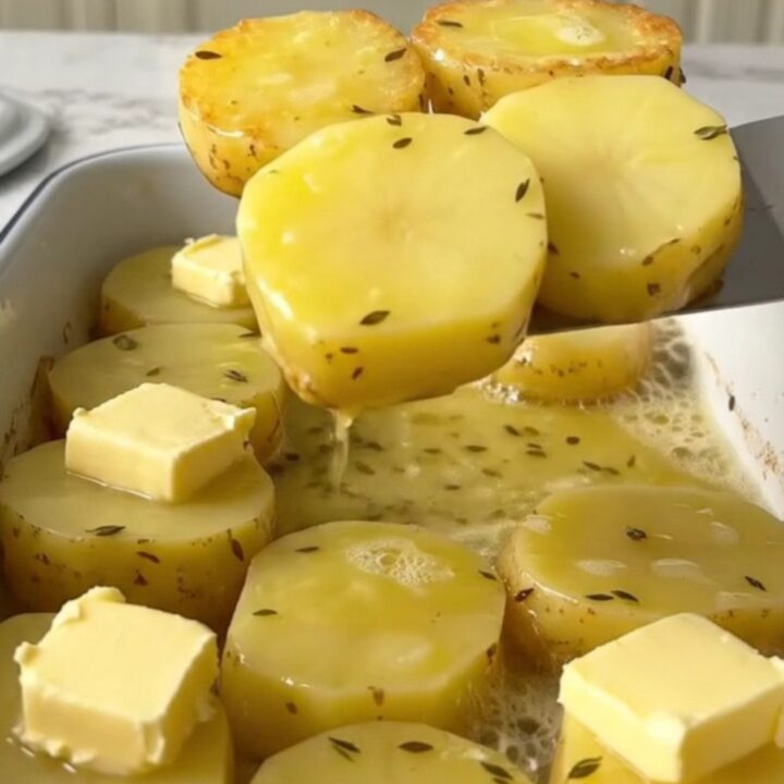 A top-down view of golden-brown melting potatoes in a white rectangular baker with fresh herbs.