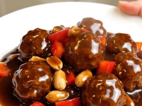 A top-down view of slow cooker kung pao meatballs with peanuts and red bell peppers.