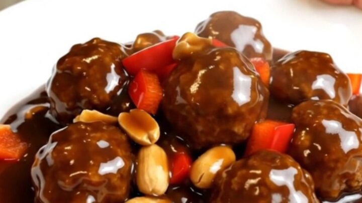 A top-down view of slow cooker kung pao meatballs with peanuts and red bell peppers.
